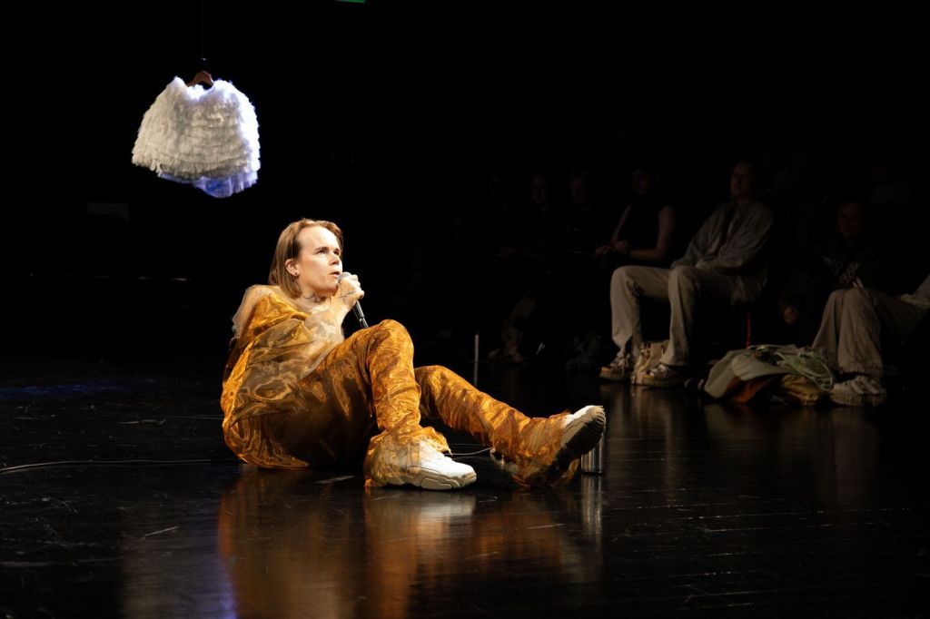 Otos Camille Auerin performanssissa Ruff Knowledge. Camille Auer lepää lavalla maaten ja pitää kädessään mikrofonia esiintymisasussaan. Kuvan on ottanut Jonne Sippola.